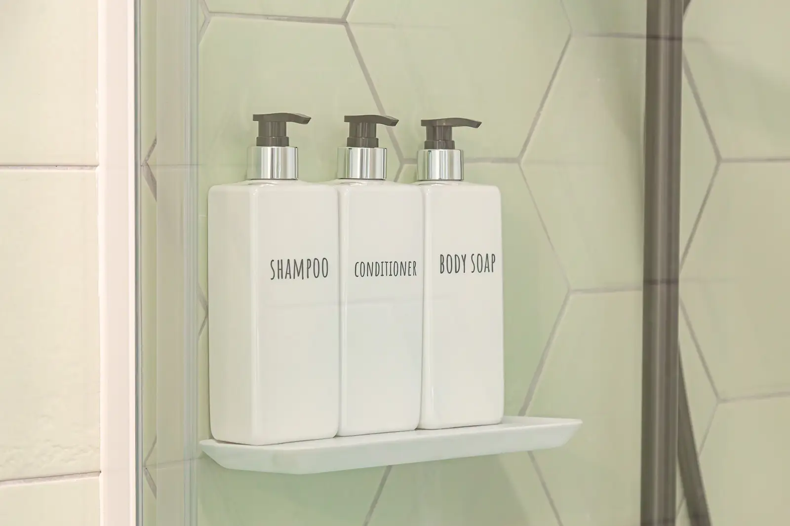 Baño con azulejos verdes con champu, acondicionador y jabon