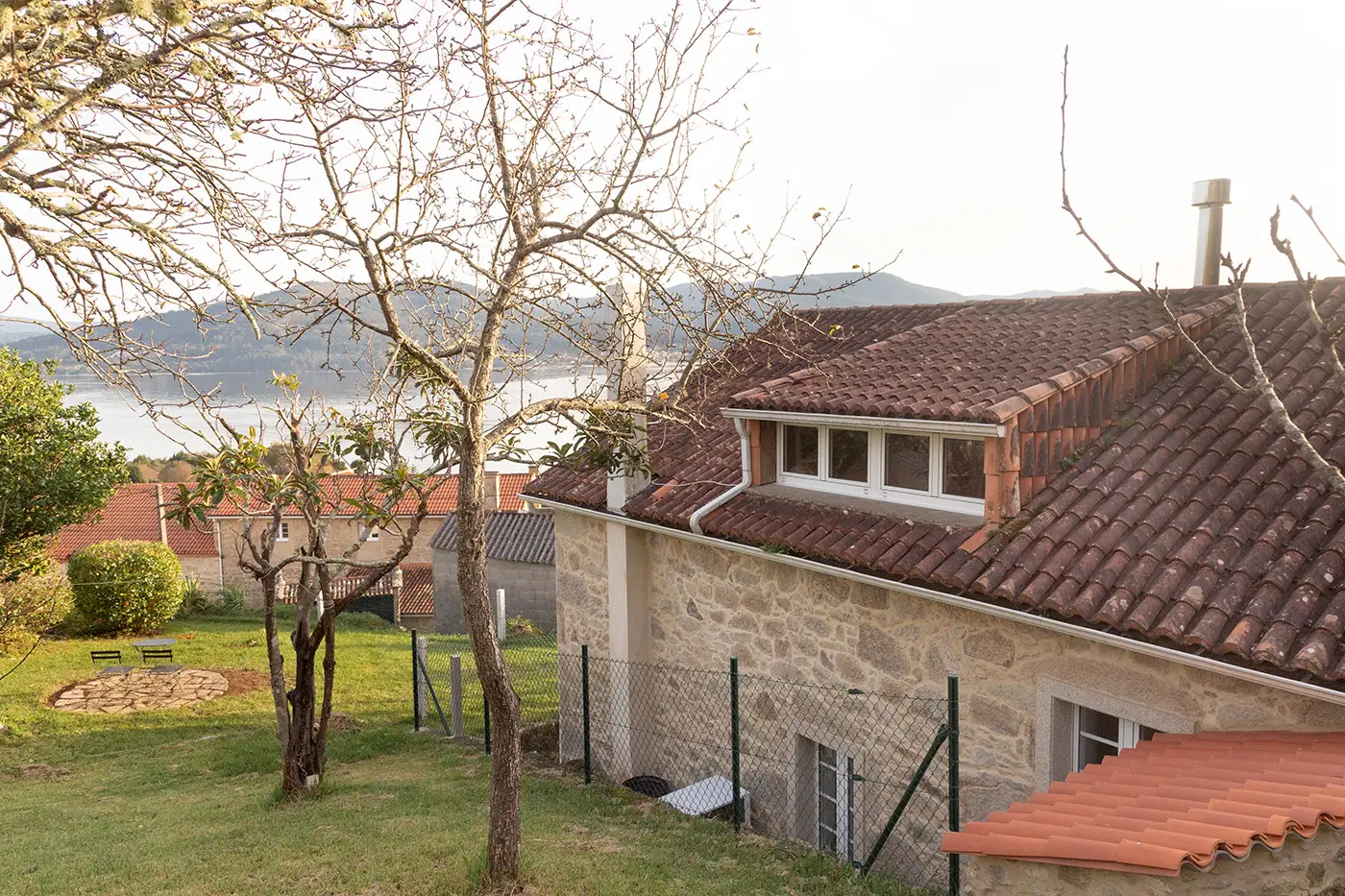 Vista exterior lateral de la casa de piedra con detalles rústicos rodeada de un entorno natural y jardines
