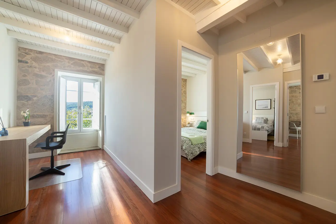 vista general de pasillo del estudio con un escritorio grande de madera un espejo de cuerpo completo y entrada a habitacion Do Porto